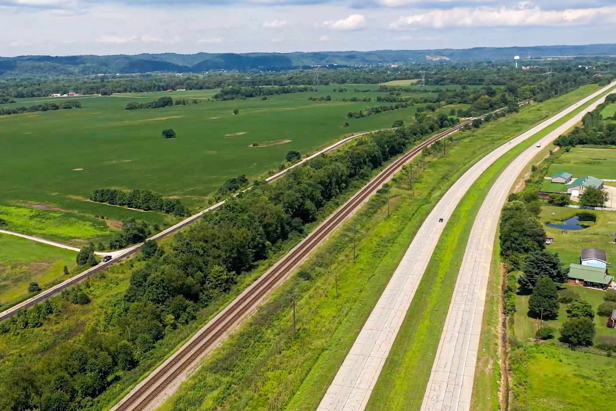Long shot of open fields next to a train track and highway showing available rail served properties for shipping metals by rail