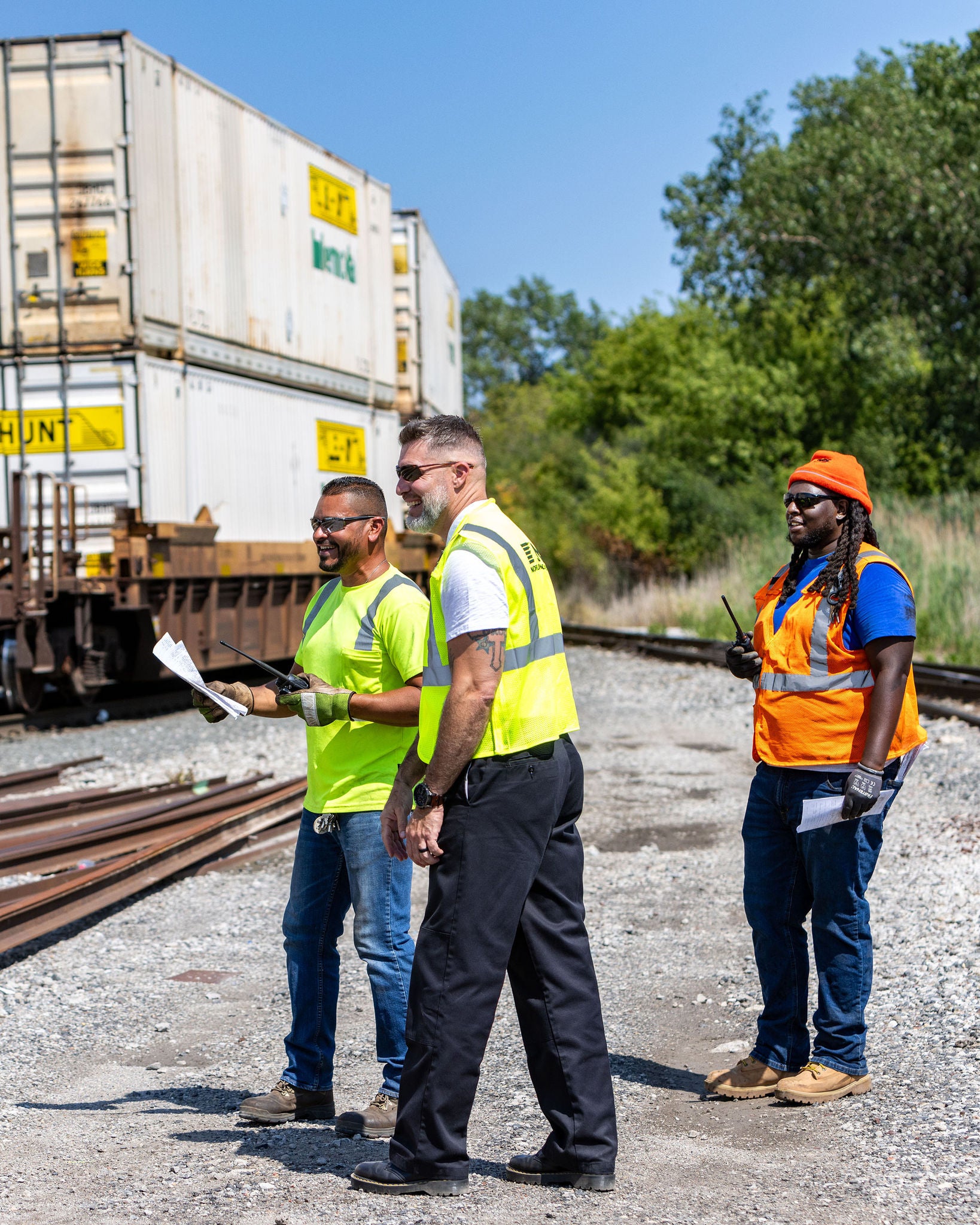 Three Norfolk Southern employees in safety vests looking at a customer centric strategy on paper next to trains