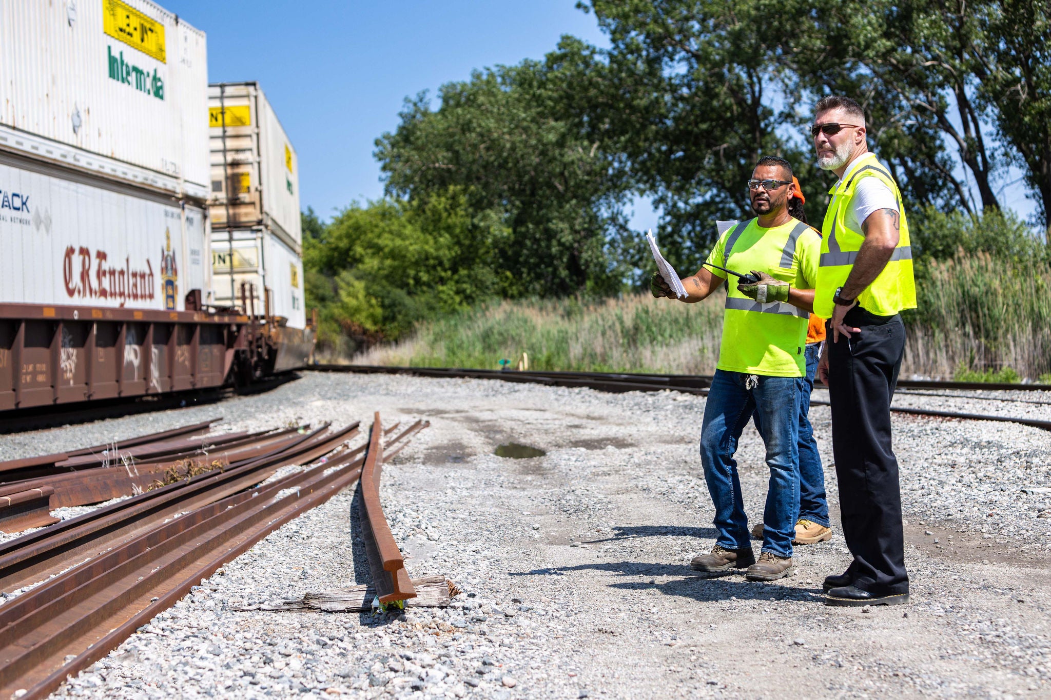 Two men looking at trains in safety vests and protective wear ready to ship by rail
