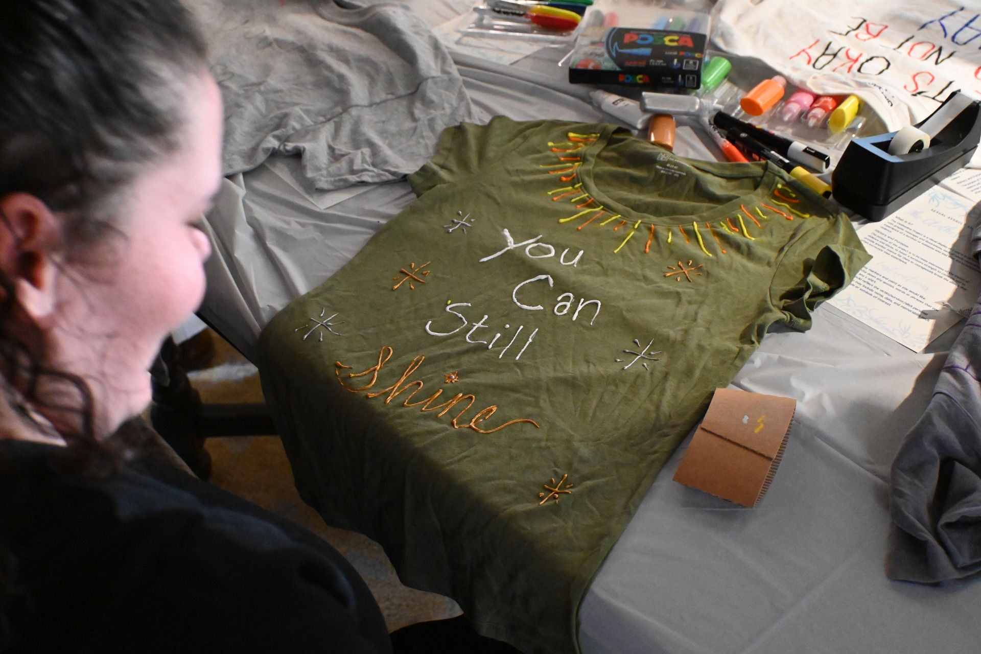 A person painting a t-shirt with the words you can still shine