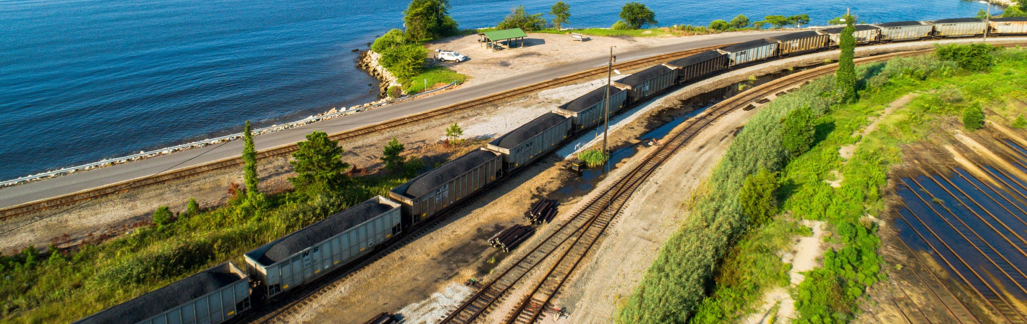 An aerial shot of Norfolk Southern’s coal shipping coal cars moving on a railway along the coast.
