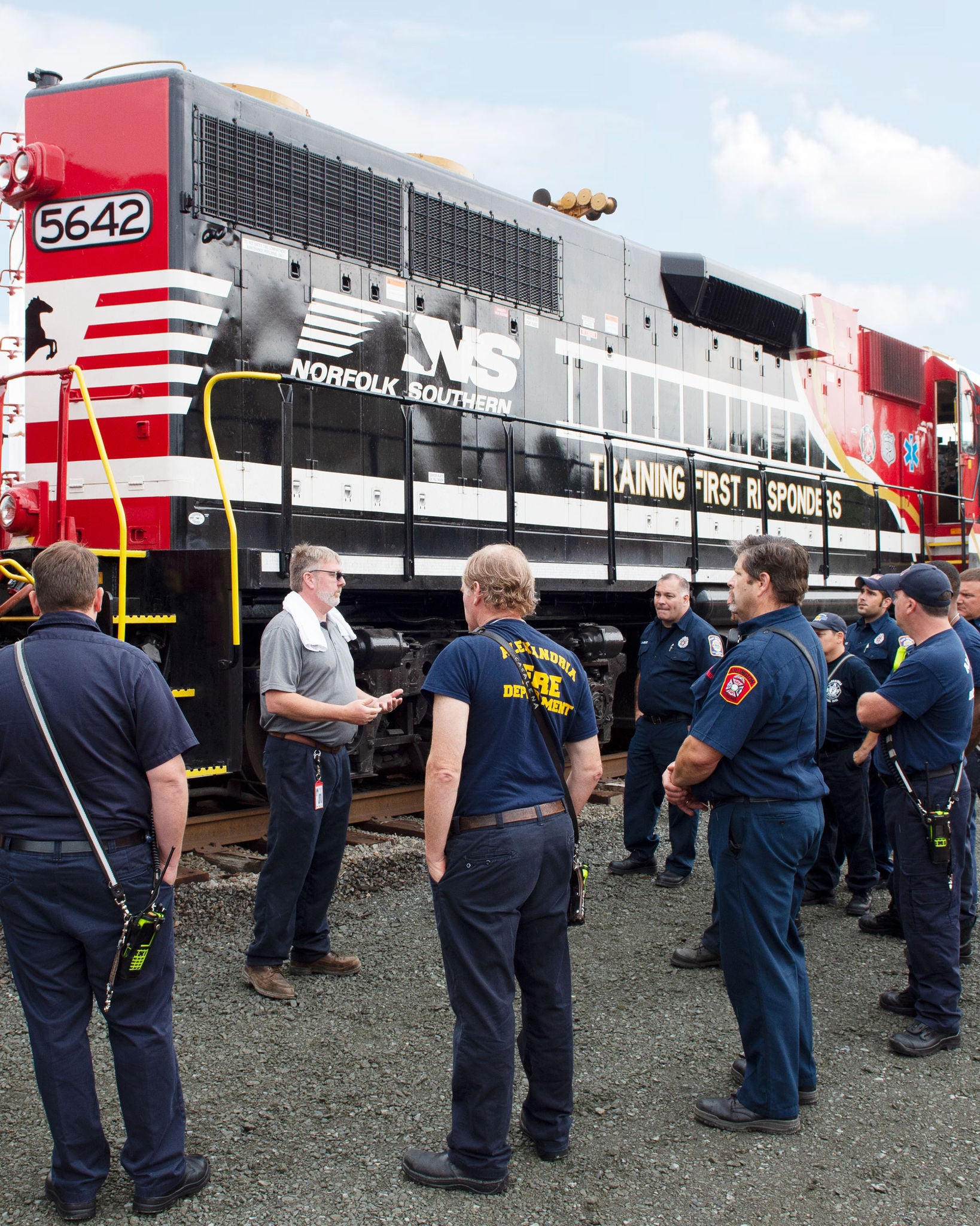 Group of first responders stand in front of a Norfolk Southern train discussing community safety