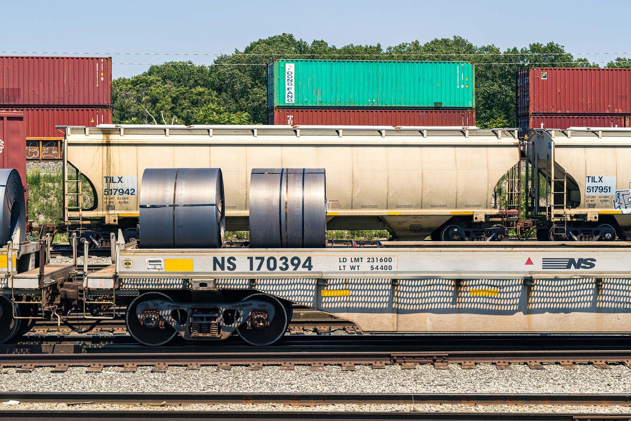 Aerial overhead shot of a Norfolk Southern employee by a train in a yard that is shipping metals by rail