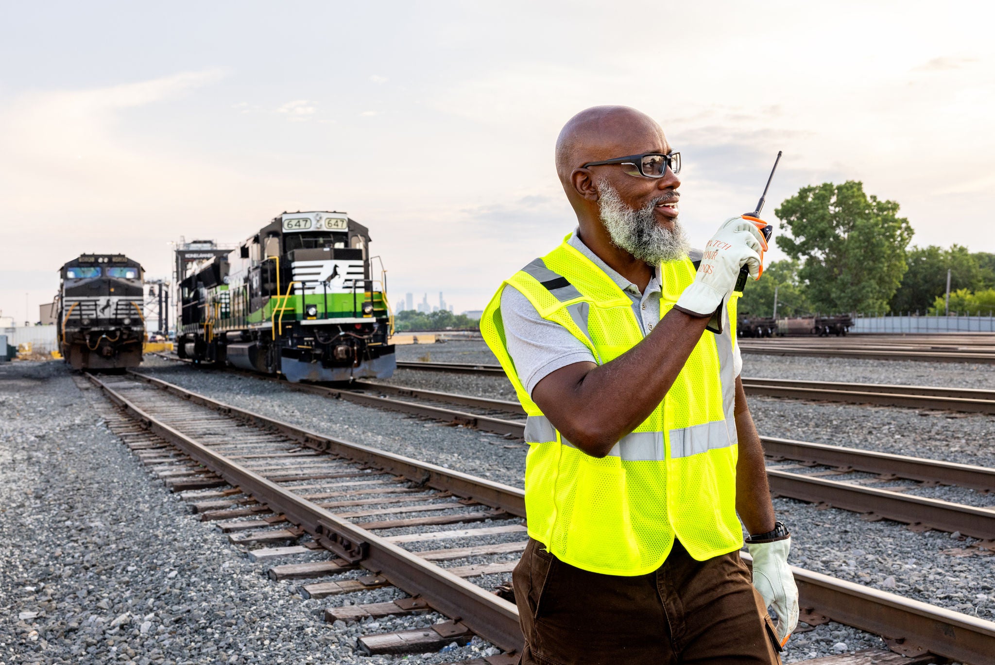 norfolk southern craft employee in railway job standing in front of locomotives with handheld transceiver