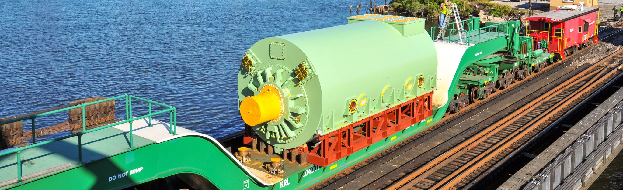 Large green object on a train on the tracks showing oversize freight shipping