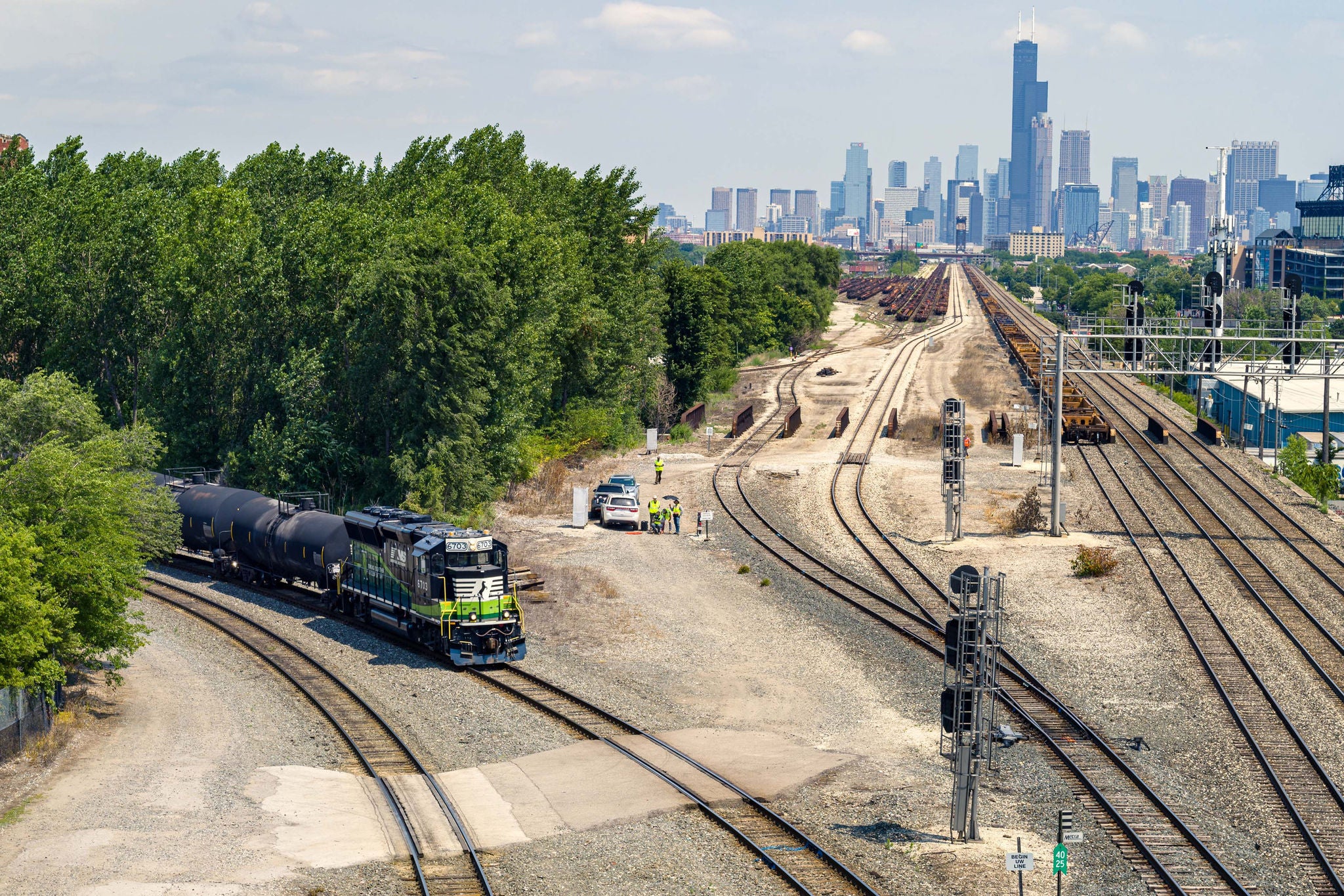 Long shot of train track with a train transporting low carbon fuels coming out of trees on the left and Chicago skyline in back