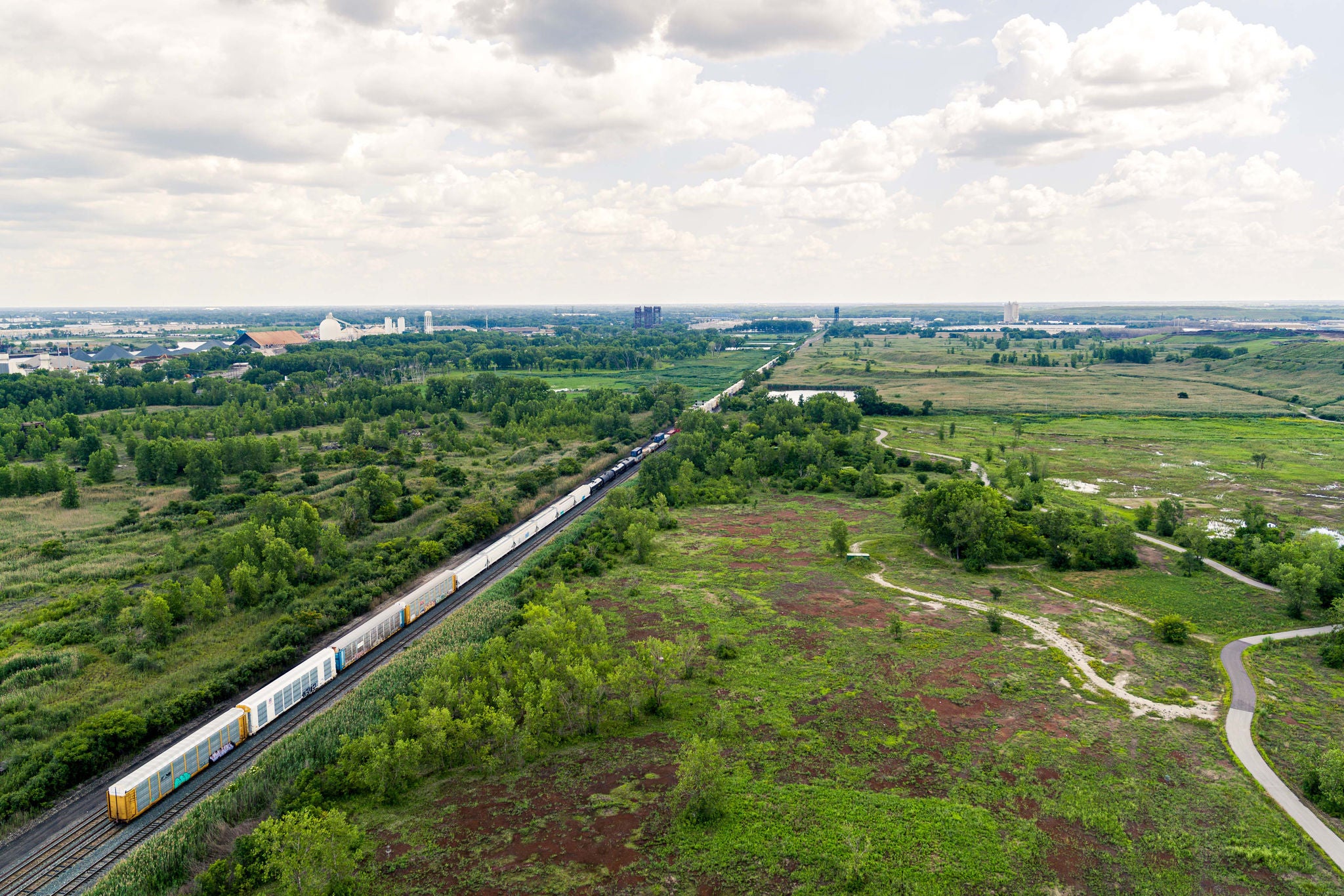Norfolk Southern train towing different types of rail shipping cars aerial view through a field